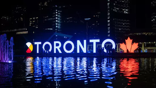 The Toronto sign lit up at night, reflecting in the water.